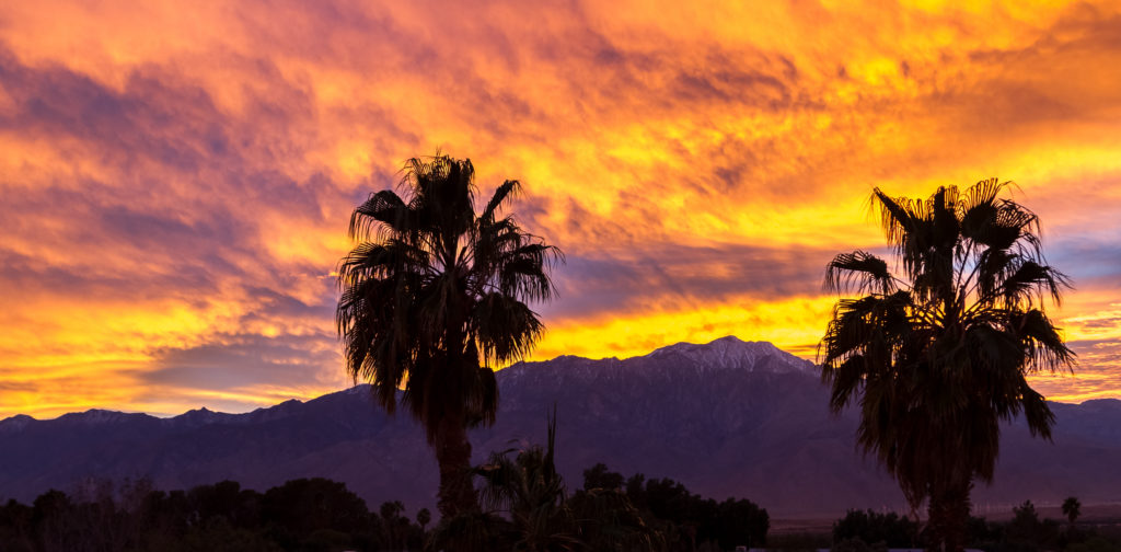 Matingkad at makulay na ulap sa itaas ng San Jacinto Mountains sa Palm Springs na may mga silhouette ng palm tree sa harapan.