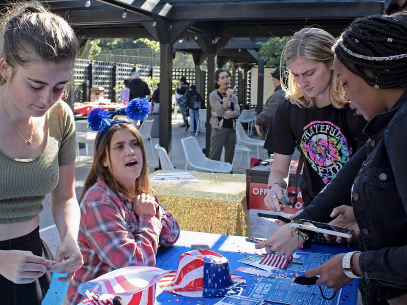 4 young people stand around a festive booth and get registered to vote.