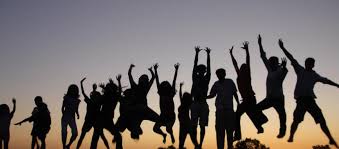 Las siluetas de un grupo de personas saltando en el aire con los brazos extendidos contra una puesta de sol.
