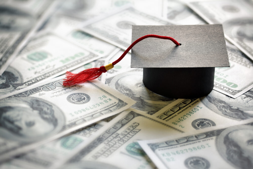Gorra de graduación que descansa sobre el concepto de billetes de cien dólares por el costo de una educación universitaria y universitaria.